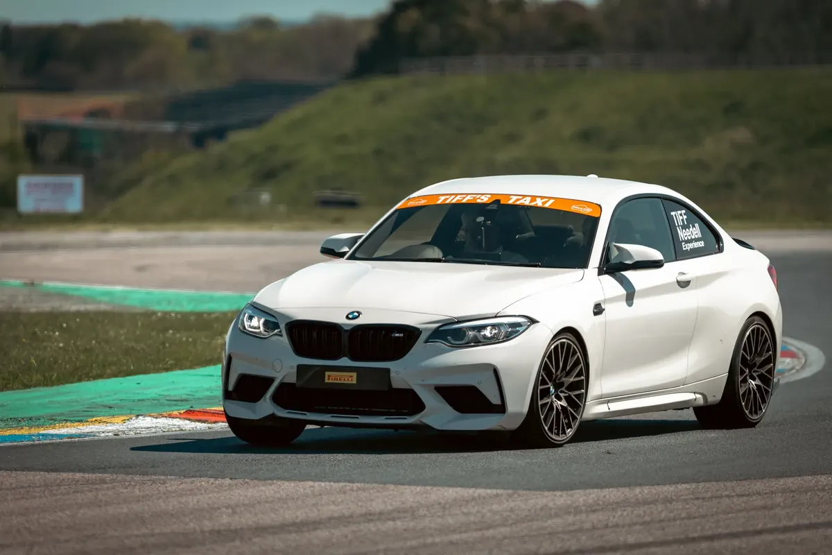 A white BMW M2 racing around a track in England on a sunny day.