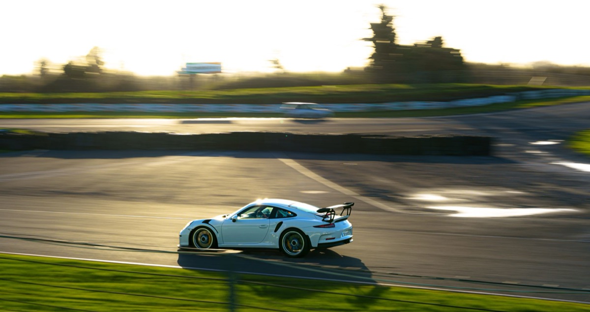 A Porsche 911 GT3 speeding through a race track during golden hour