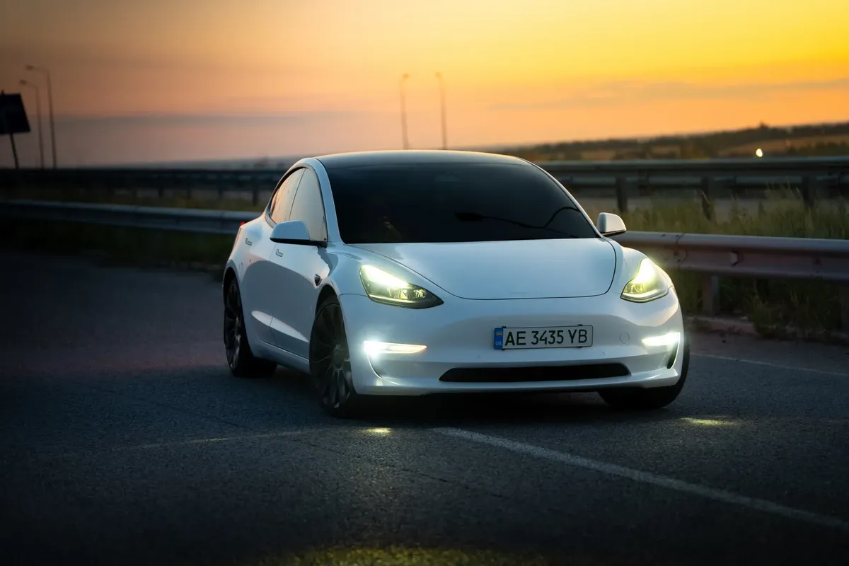 Sleek white electric car driving on a highway during a stunning sunset in Dnipro, Ukraine.