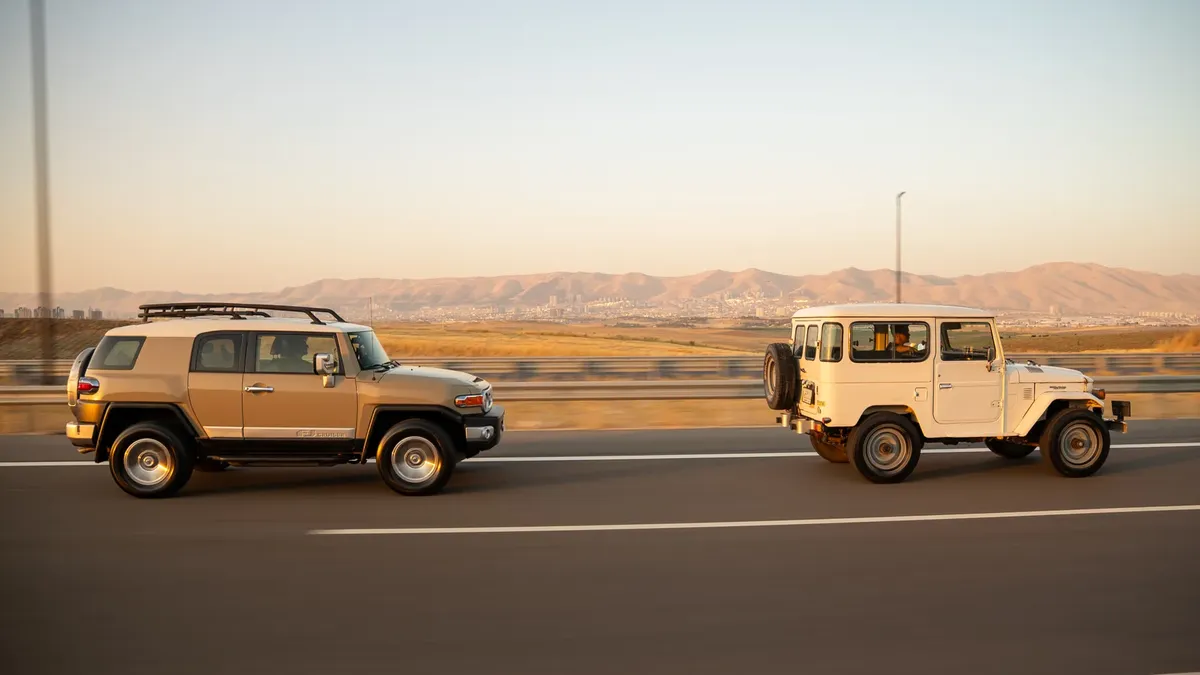 Two SUVs driving on a highway near mountains during daylight.